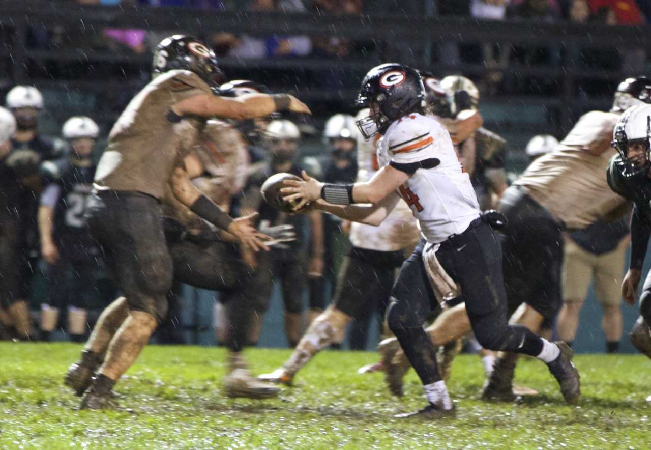 Gladstone quarterback Hudson Meyer (14) hands off against Estacada. (Photo by Sarah Murch-Hill)